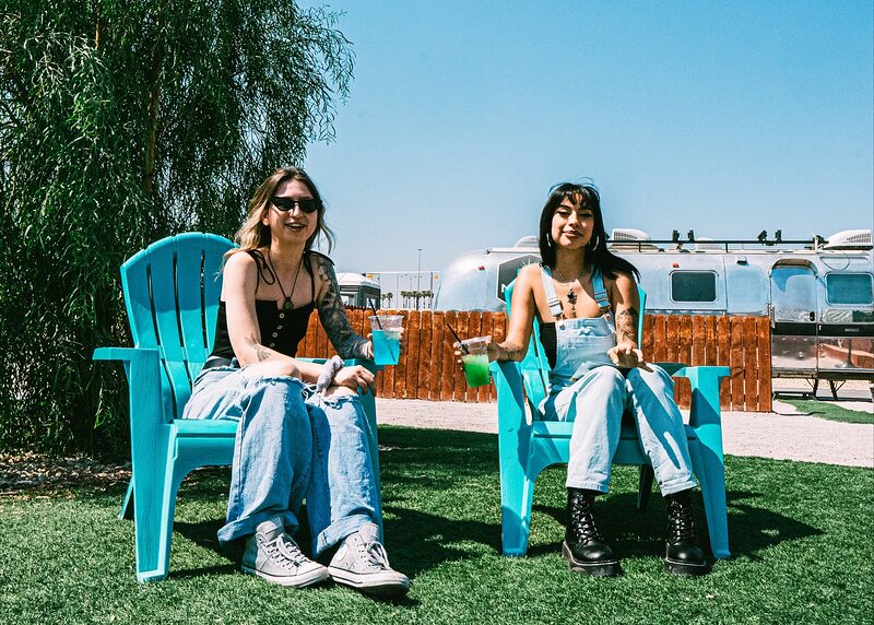 Two friends in turquoise Adirondack chairs with cannacocktails under a blue desert sky