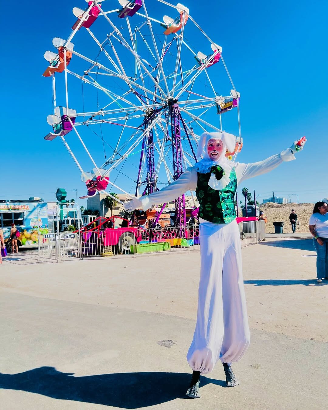 A stilt-walker in cotton-candy stripes towers beside the ferris wheel