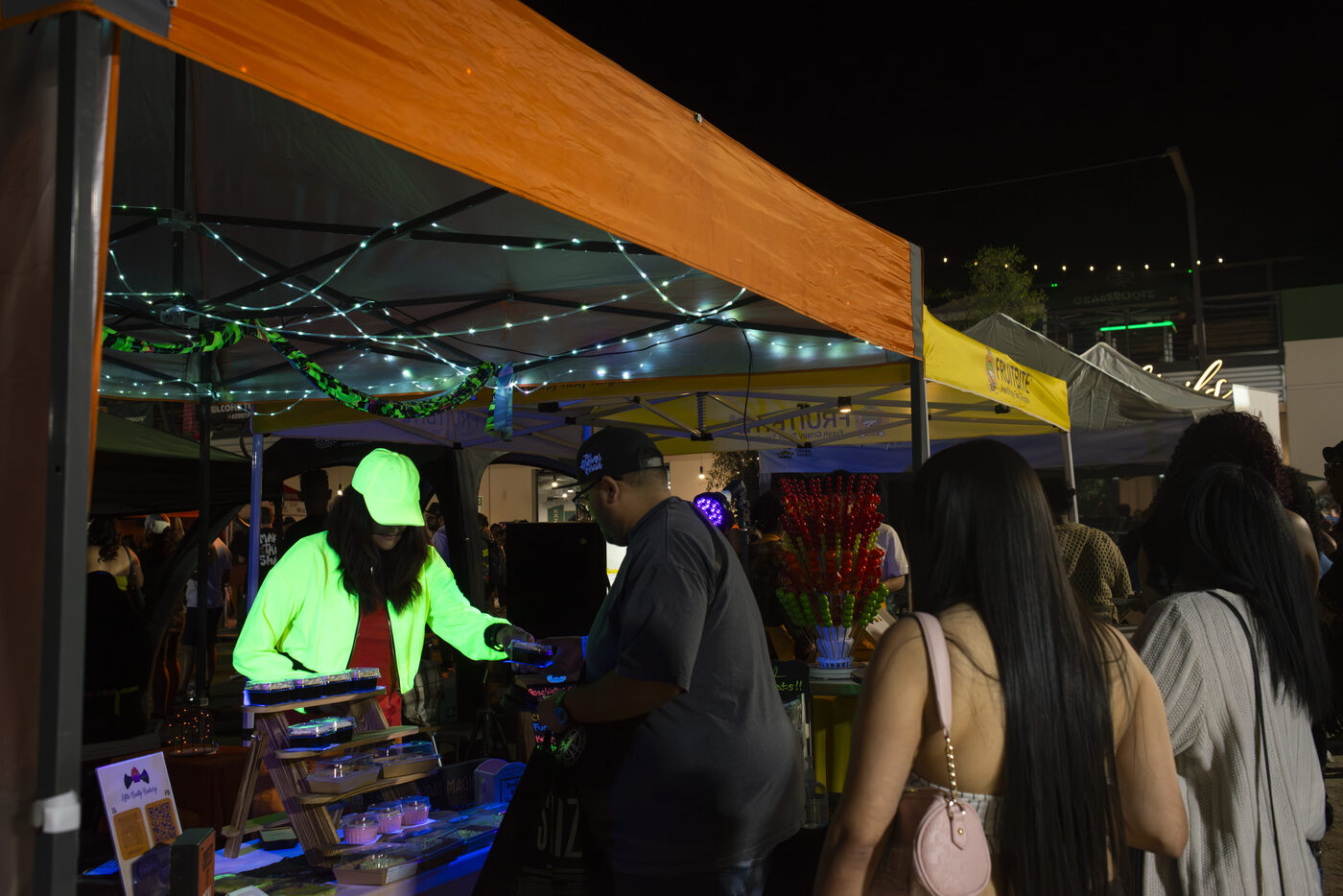A vendor serves guests at a glowing booth after dark